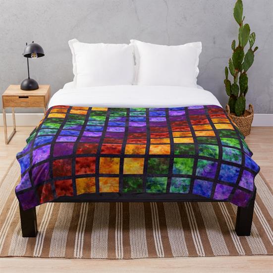 A throw blanket featuring a rainbow spectrum square quilt design outlined in black..