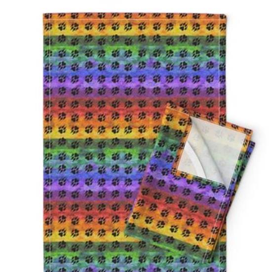 Tea towels with a mottled rainbow and repeated paw print design.